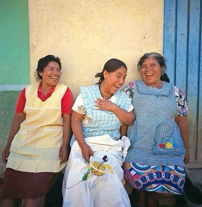 Tres mujeres artesanas riendo juntas frente a una pared de colores
