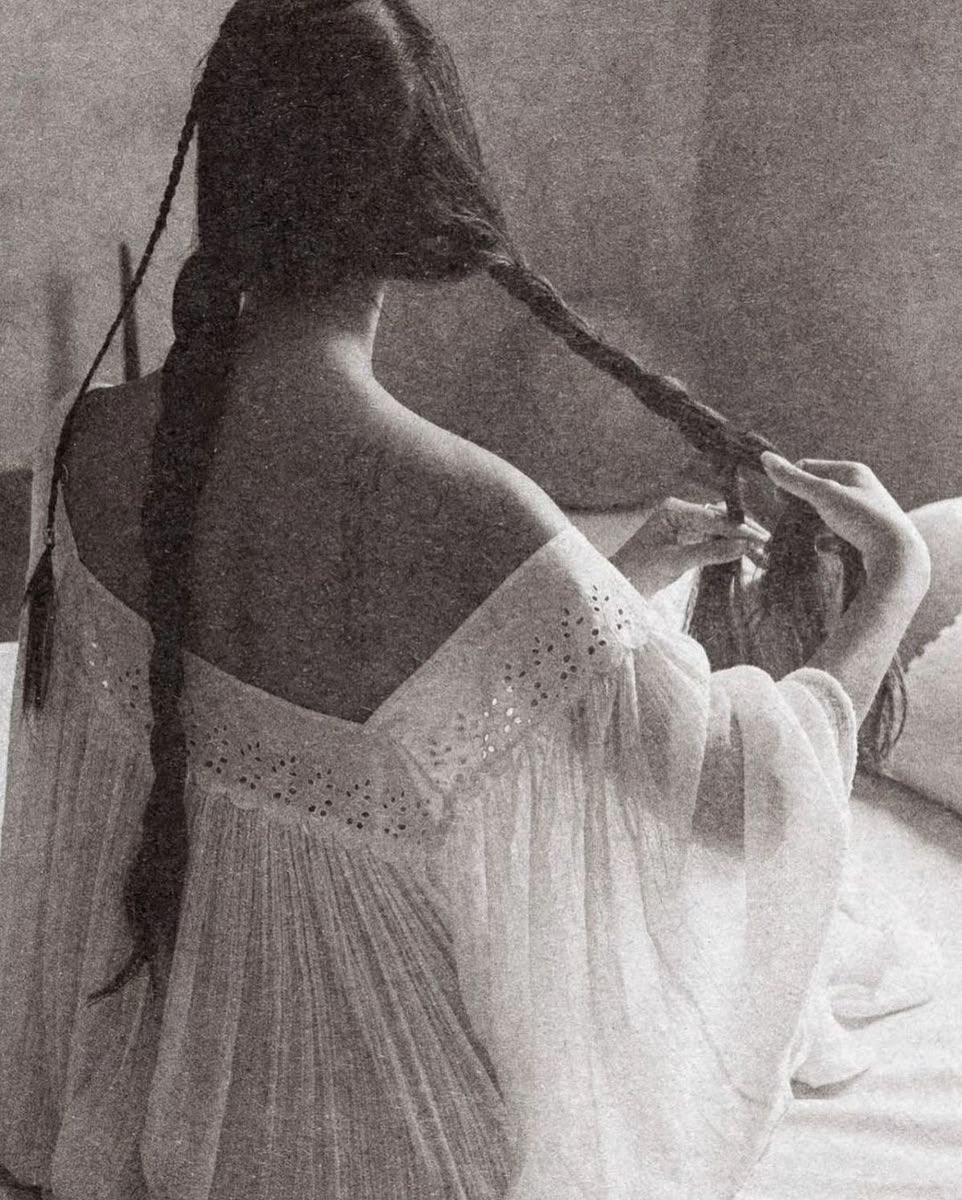 Una mujer de espaldas trenzándose el cabello, en blanco y negro